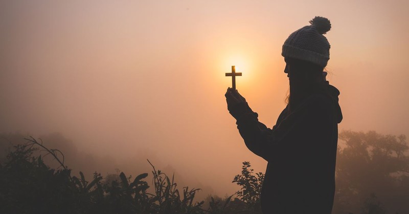 Woman praying at sunset while holding a small cross